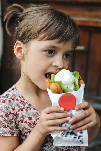 女の子は屋外で果物とワッフルの泡とアイスクリームを食べています。