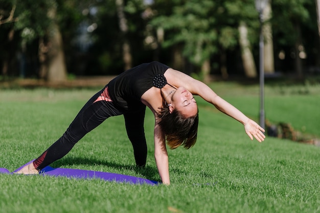 The girl is engaged in yoga in the park on the grass. A woman performs asanas in the park in the summer.