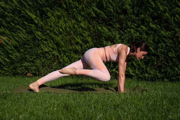 Una ragazza è impegnata nello yoga per strada, in una tuta rosa fa vari esercizi e pose yoga