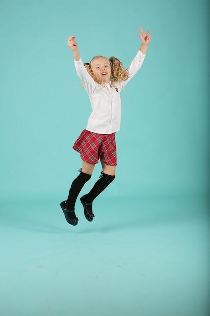 a girl is a happy blonde in a shirt and a plaid skirt a schoolgirl jumps