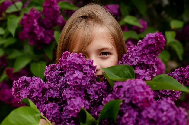 A girl is hiding behind a lilac bush.