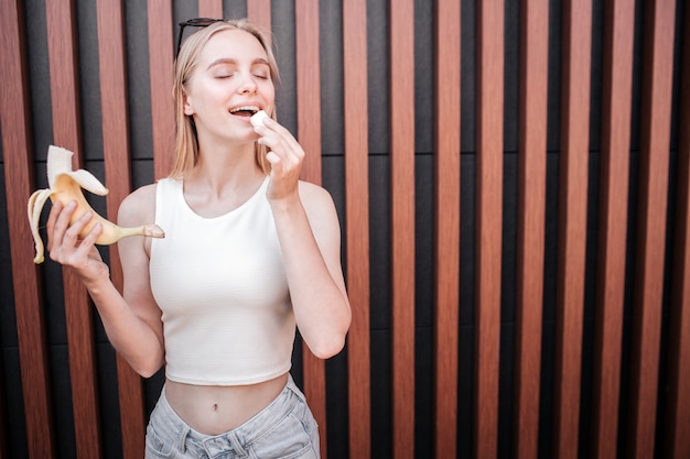 Girl is holding banana in one hand and a piece of it in the other one.