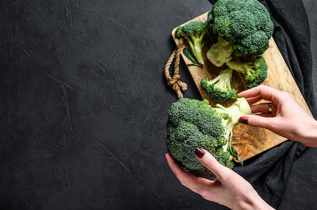 The girl is holding a fresh broccoli. Black background. Top view. Space for text.