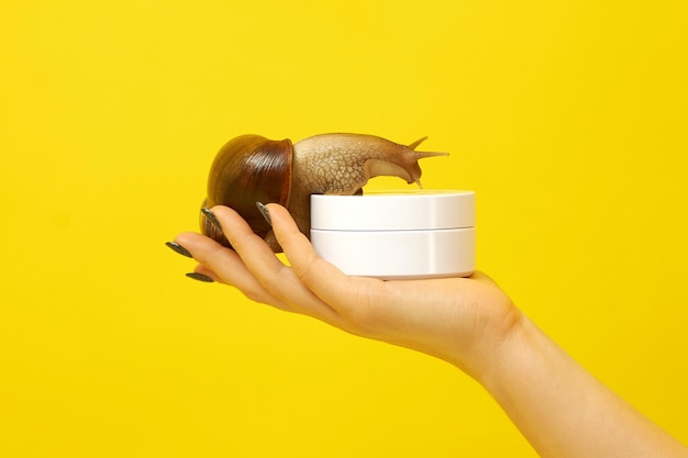 The girl is holding a jar and a snail on her hand