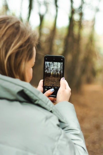 девушка держит мобильный телефон и фотографирует природу, осенний пейзаж, оцифровку