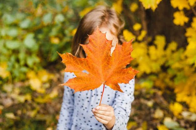 The girl is holding an orange maple leaf in her hand