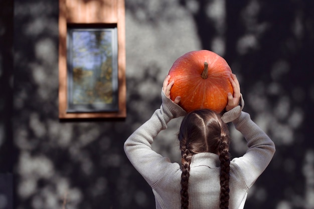 Photo girl is holding an orange pumpkin under her head in the garden fresh vegetables in child hands