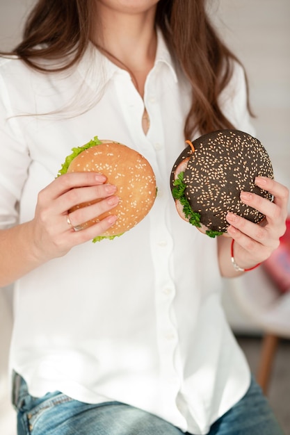 The girl is holding two sandwiches and is hesitant whether to eat them for a good figure and health