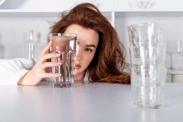 Foto una ragazza sta guardando attraverso un bicchiere d'acqua distorcendo visivamente il suo viso dimostrando prodotto vitamine idratanti bevande alcoliche