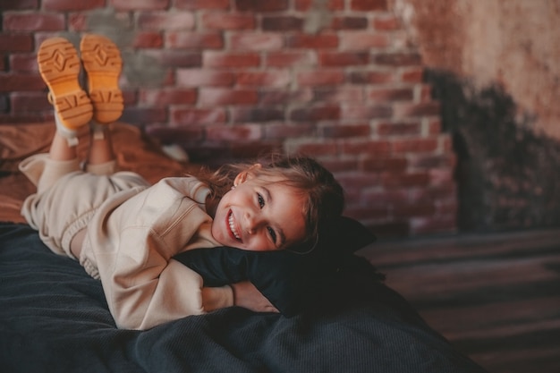 the girl is lying on the bed on the background of a brick wall