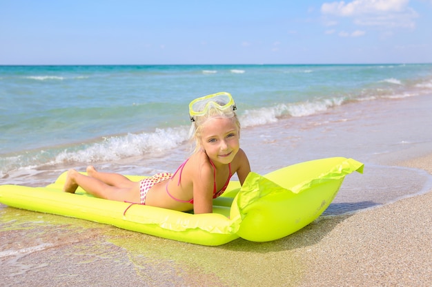 Girl is lying on yellow inflatable with googles and scuba diving on the beach