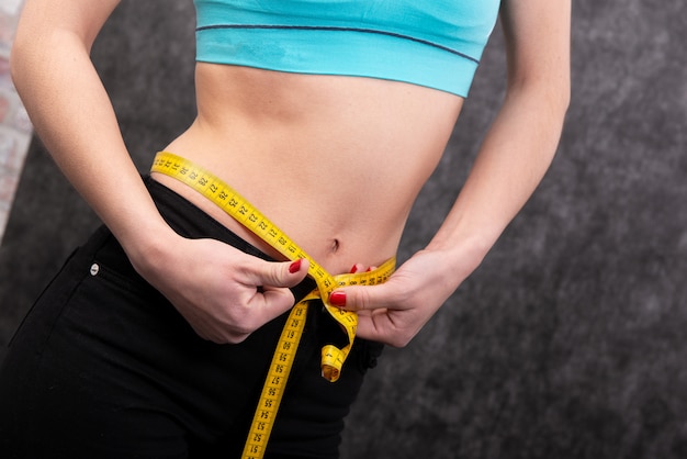 Girl is mesuring her waist with measuring type. Close-up