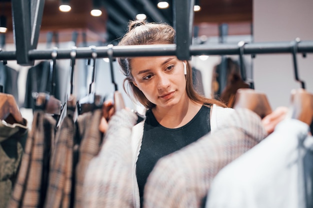 女の子は新しい服を着てモダンな店にいますエレガントな高価な服