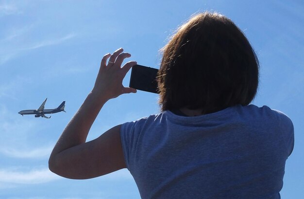 Девушка фотографирует самолет, летящий в небе