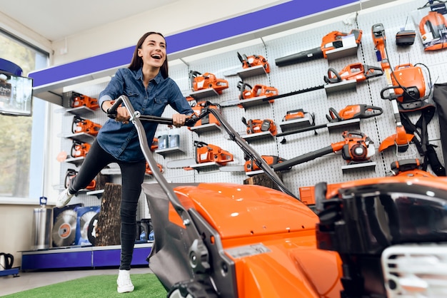 A girl is posing with a lawn mower in a tool store.