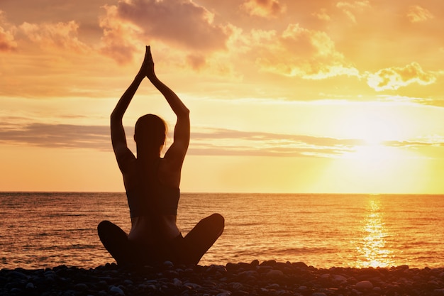 Girl is practicing yoga on the beach. View from the back, sunset, silhouettes