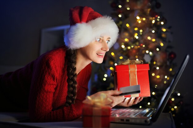 소녀는 크리스마스를 준비하고 신용 카드를 사용하여 인터넷을 통해 선물을 주문합니다
