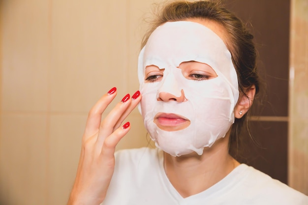 Girl is putting skin mask sheet on face beauty procedures at\
home