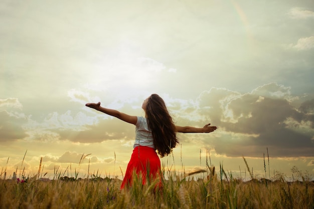 Girl is raising her arms and enjoys with nature. Fleshy wheat ears on the fields, summer crop