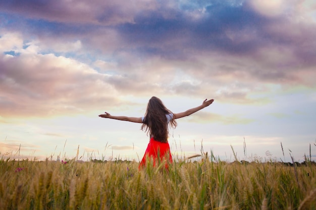 Girl is raising her arms and enjoys with nature. Fleshy wheat ears on the fields, summer crop