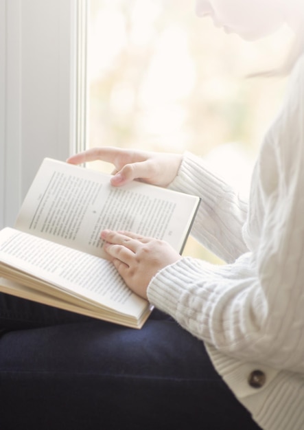 Girl is reading book beside window