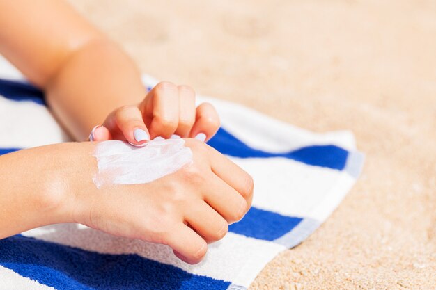Photo girl is relaxing on the towel on the sand at the beach and applying sun lotion on her hand.