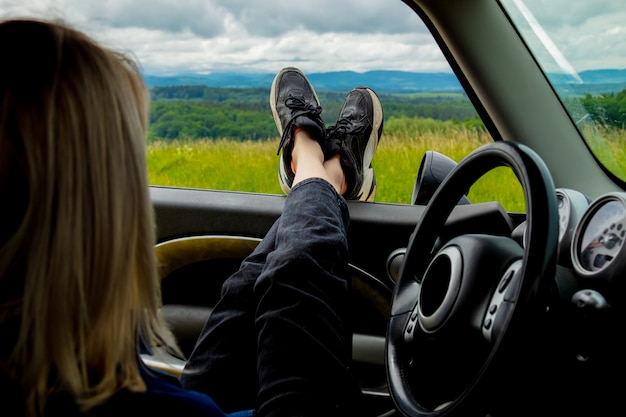 여자는 창 밖으로 그녀의 발로 차에 앉아있다, 산