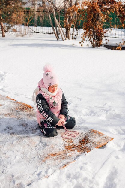 Girl is sitting on carpet in winter child learns to clean carpet by traditional method with help of ...