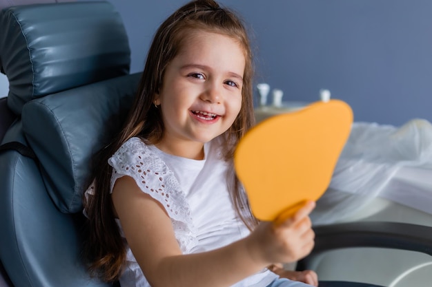 A girl is sitting in a chair and holding a yellow mirror.