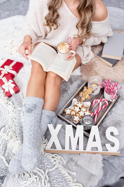 The girl is sitting in a christmas atmosphere, drinking a hot drink and reading a book.