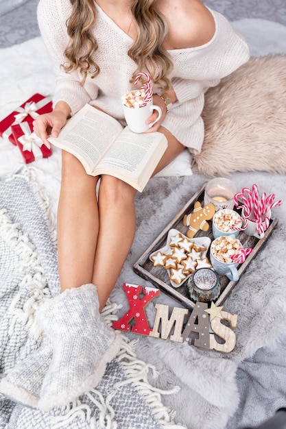 The girl is sitting in a christmas atmosphere drinking a hot drink and reading a book