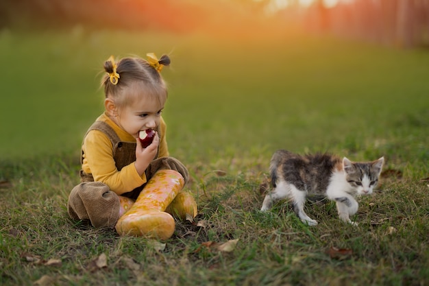 한 소녀가 새끼 고양이와 함께 해질녘 정원의 잔디에 앉아 있다
