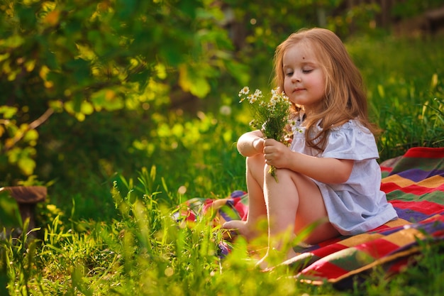 a girl is sitting on the green grass and sniffing chamomile nature in the village