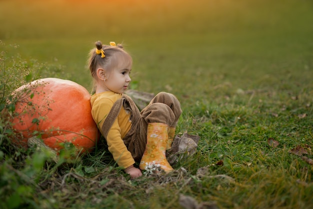 A girl is sitting on the ground with her back against a large pumpkin