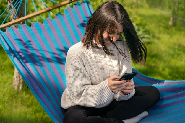 Girl is sitting in hammock with phone in hand and writes message