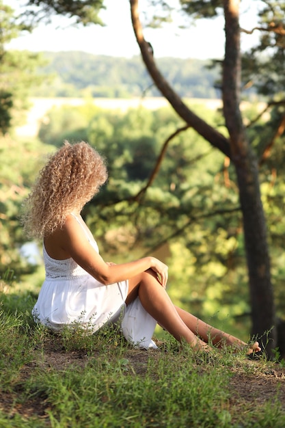 The girl is sitting on the outskirts of the field and looking into the distance