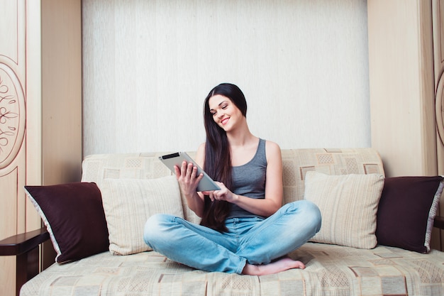 A girl is sitting with a tablet on a beige couch