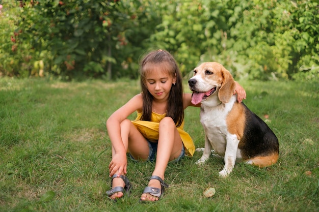 A girl is sitting in yard on lawn with beagle dog