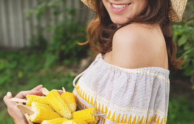 The girl is smiling in a straw hat and holding a plate of boiled corn in her hands The concept of outdoor recreation barbecue Noise effect