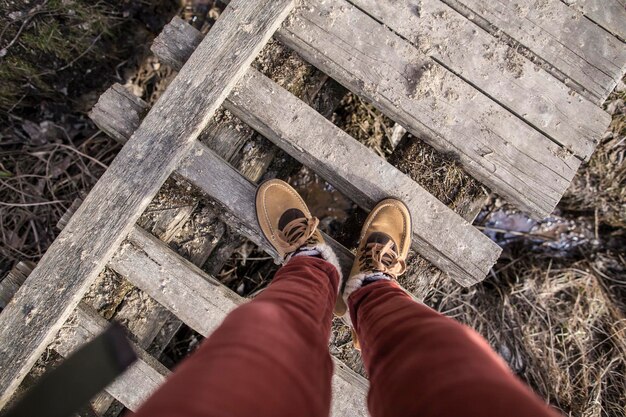 Girl is standing on an old rotten wooden bridge in stylish boots on sunny afternoon Top view