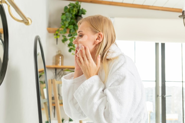 a girl is standing sideways looking in the mirror, a young woman is taking care of her facial skin