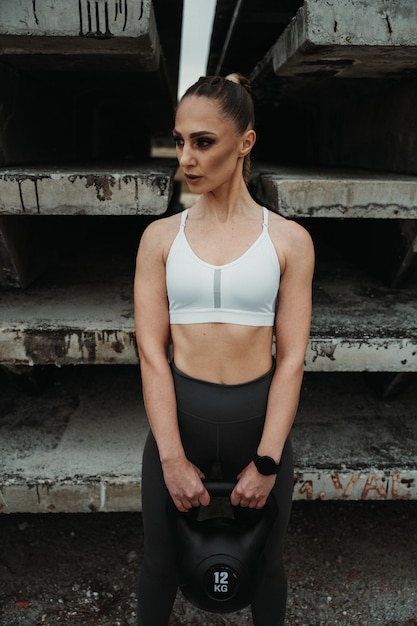 A  girl is standing straight and holding a dumbbell with a look to the right side and a smart watch