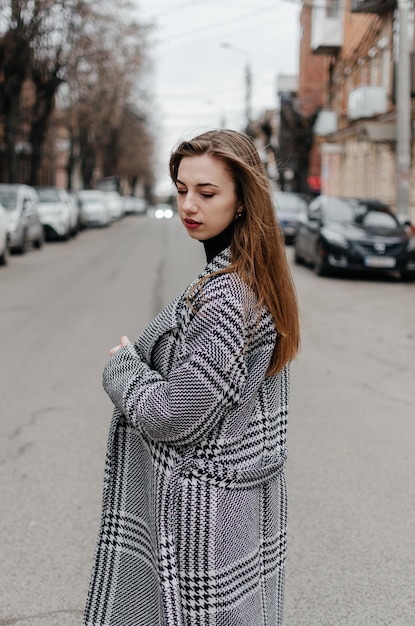 The girl is standing on the street in a gray coat