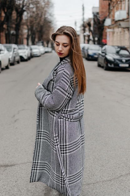 The girl is standing on the street in a gray coat