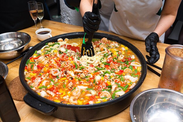 Photo a girl is stirring paella with a black plastic spatula a large paella bowl on the table