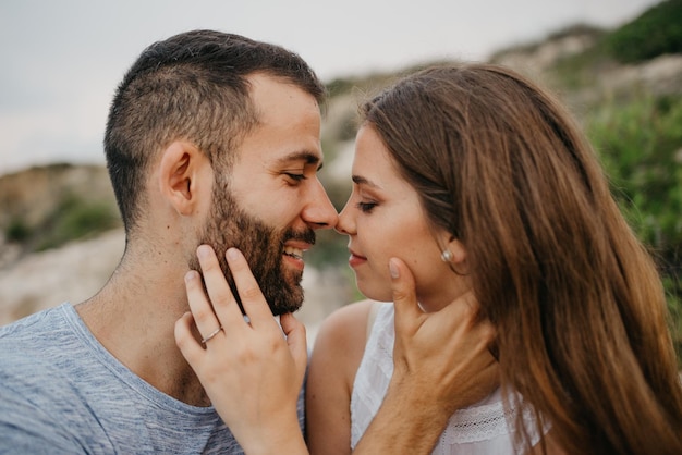 A girl is stroking with her hands the face of her boyfriend on the rocky hill