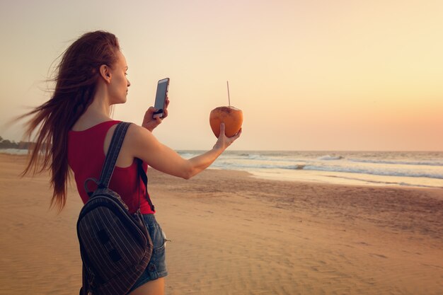 A girl is taking pictures of a coconut on the sunset