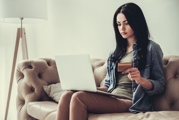 Girl is using laptop and holding a credit card.