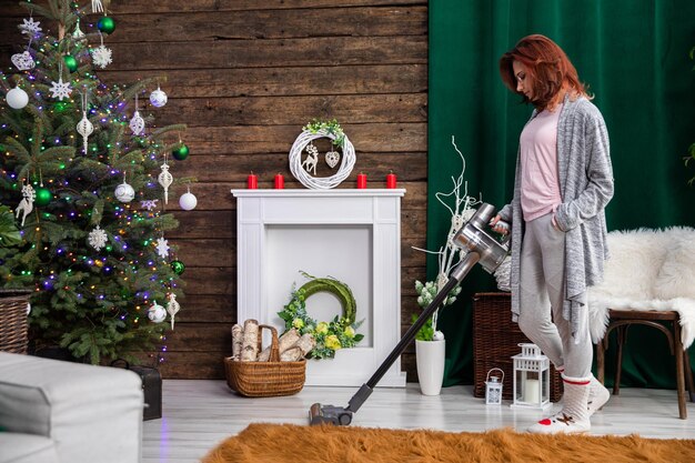 Photo the girl is vacuuming in the living room decorated for christmas