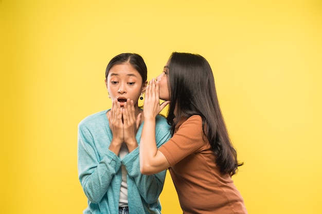 A girl is very shocked when her friend talks whispering in her ear